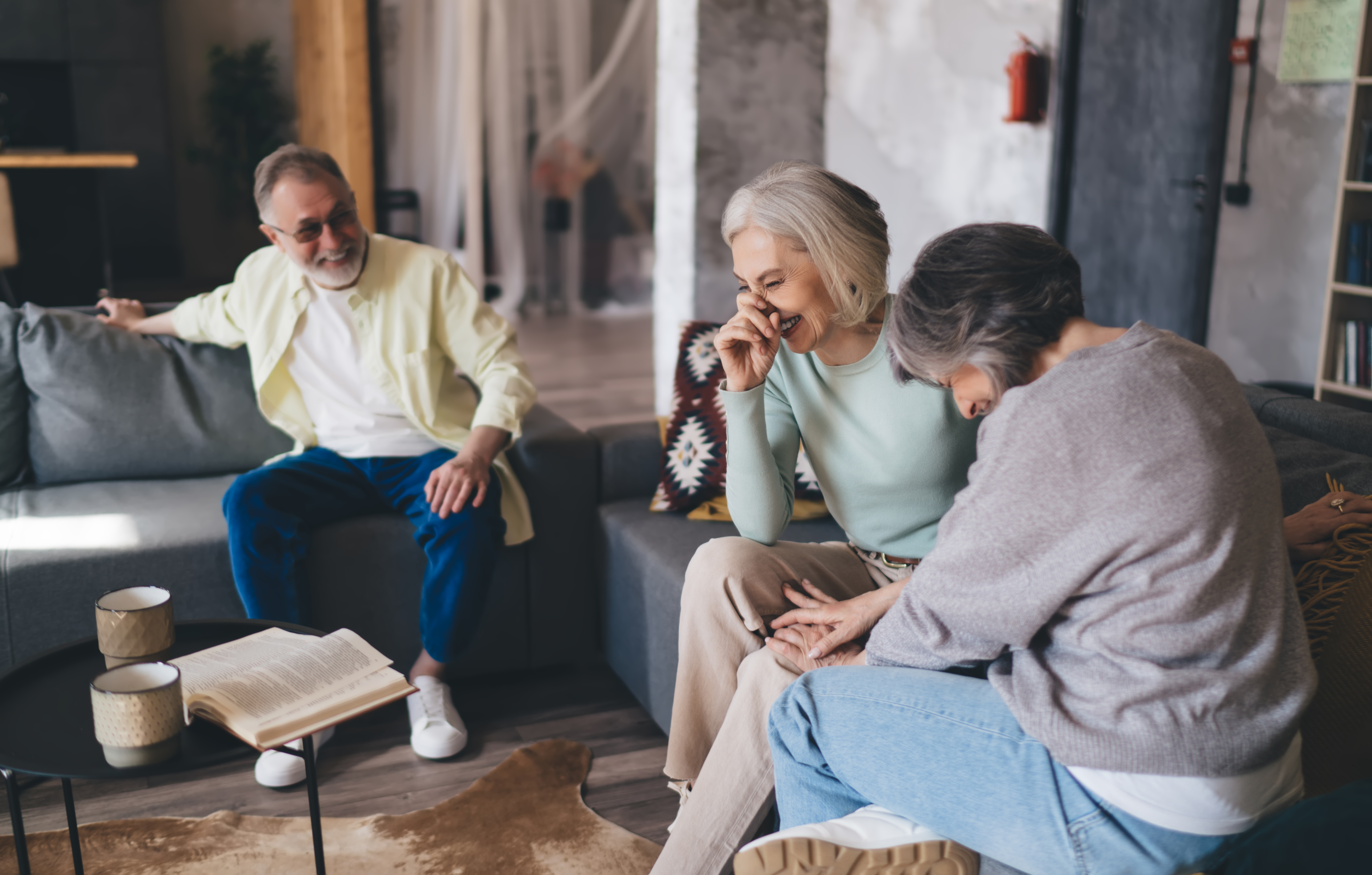 Happy middle aged women and man sitting on sofa and laughing in living room