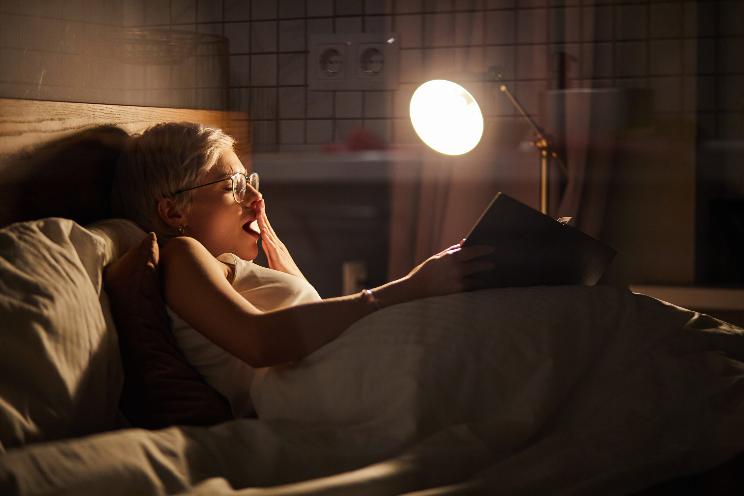 woman yawning while reading in bed at night