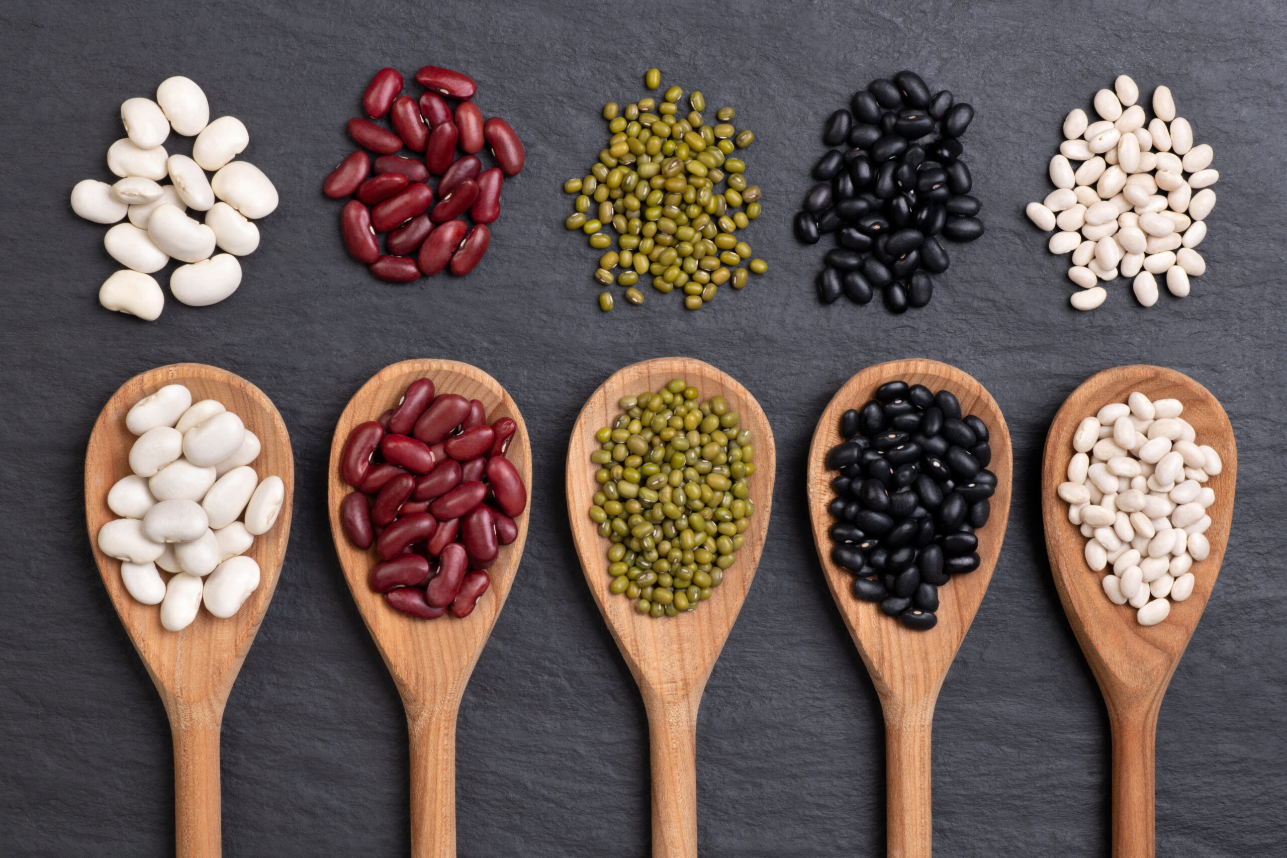 Beans selection in spoons on black background, top view
