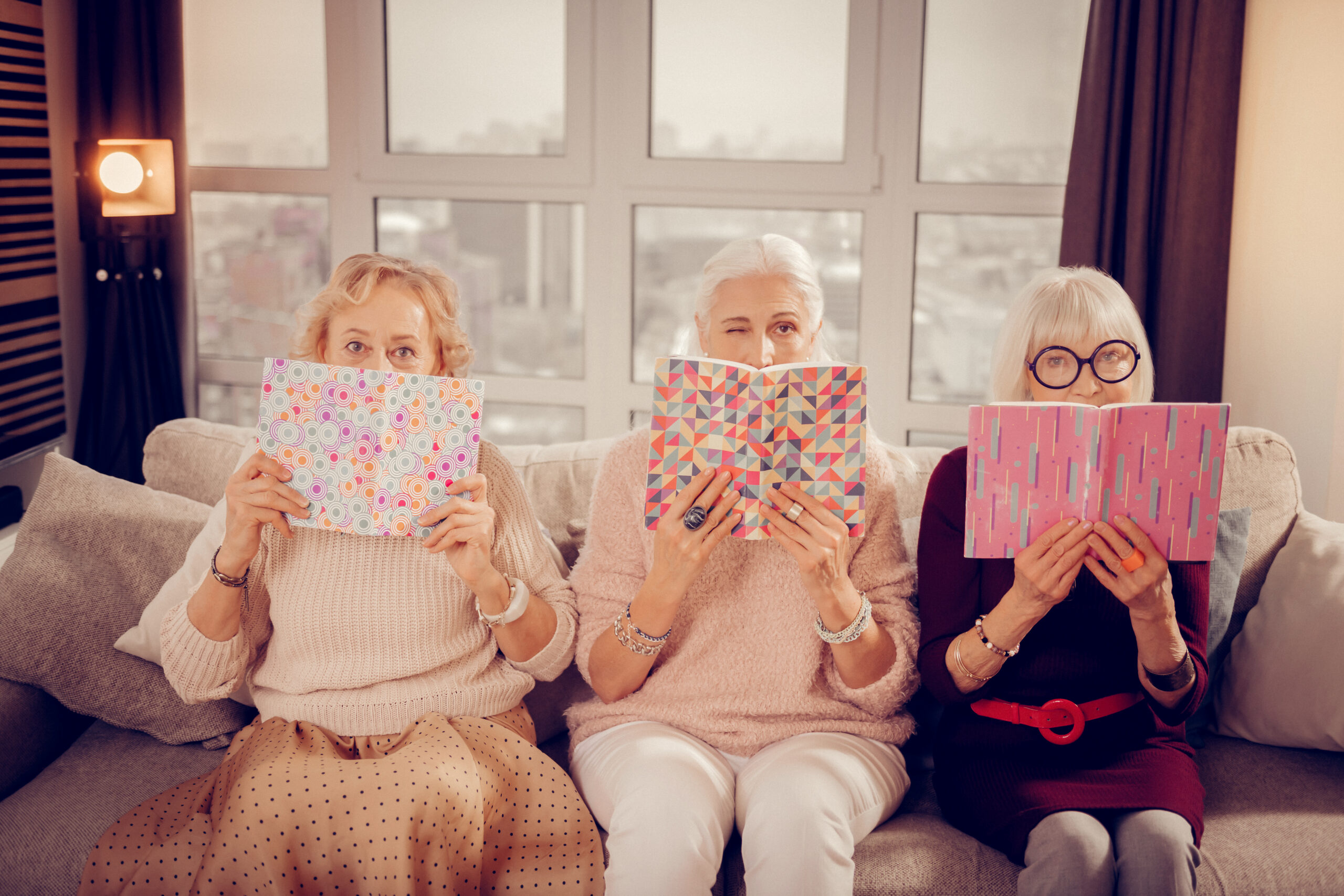 Join us. Nice aged woman winking at you while holding a book in front of her