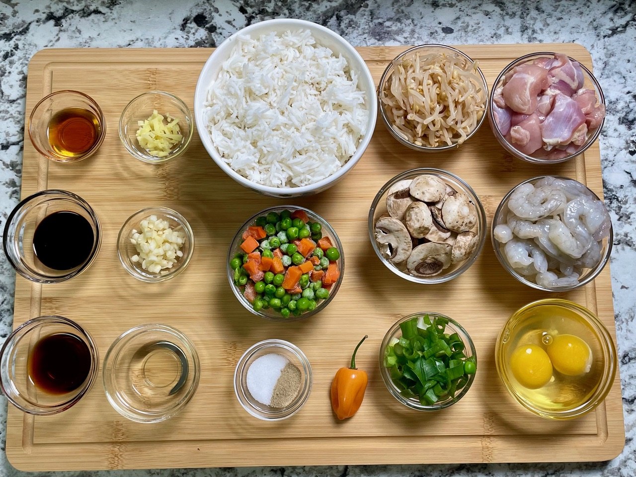 Mis en place for chicken and shrimp fried rice with measured ingredients in small bowls on a cutting board