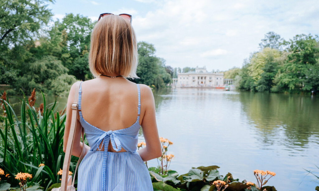 Attractive blonde woman looking at palace and lake in park in Warsaw