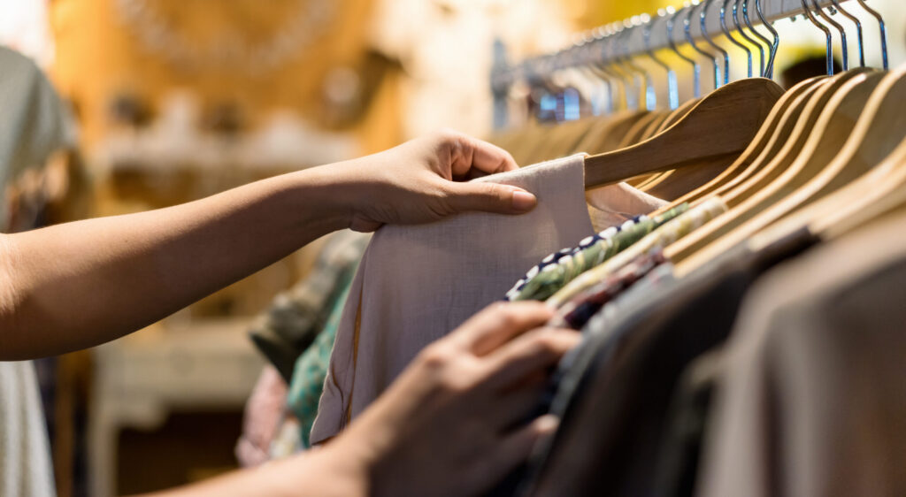 Close up of woman hand choosing clothes in store, searching or buying shirt on rack hanger at flea market , stall shopping apparel fashion concept