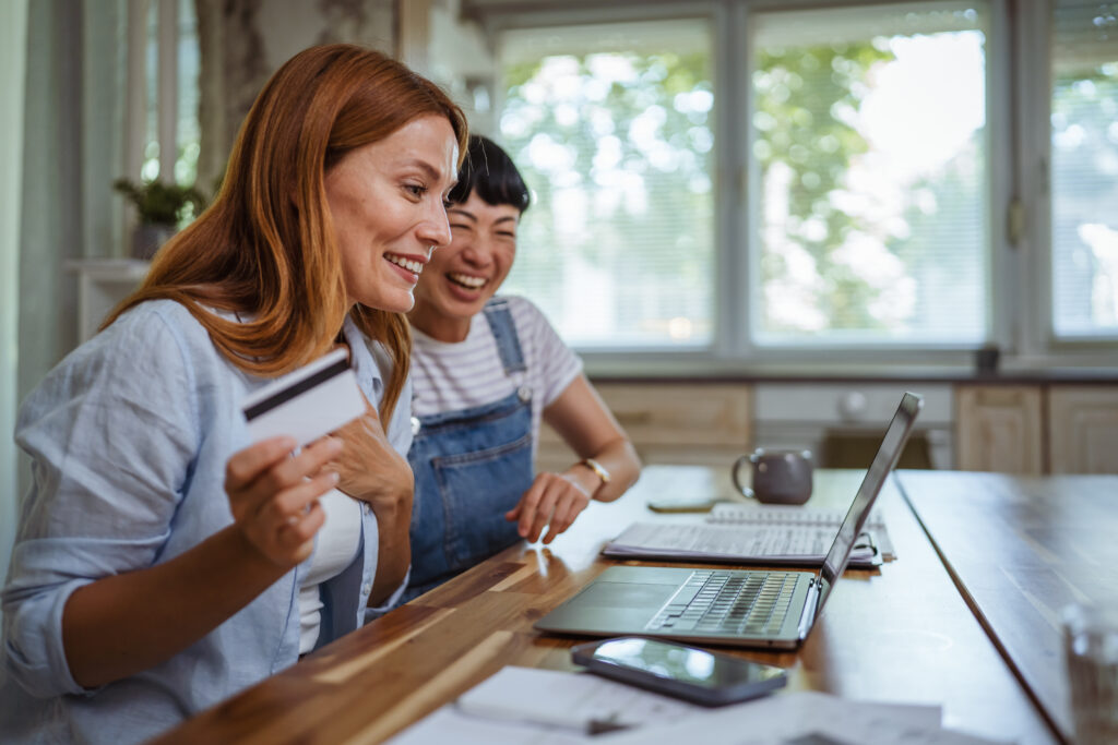 Happy japanese and caucasian woman buy online on laptop from home