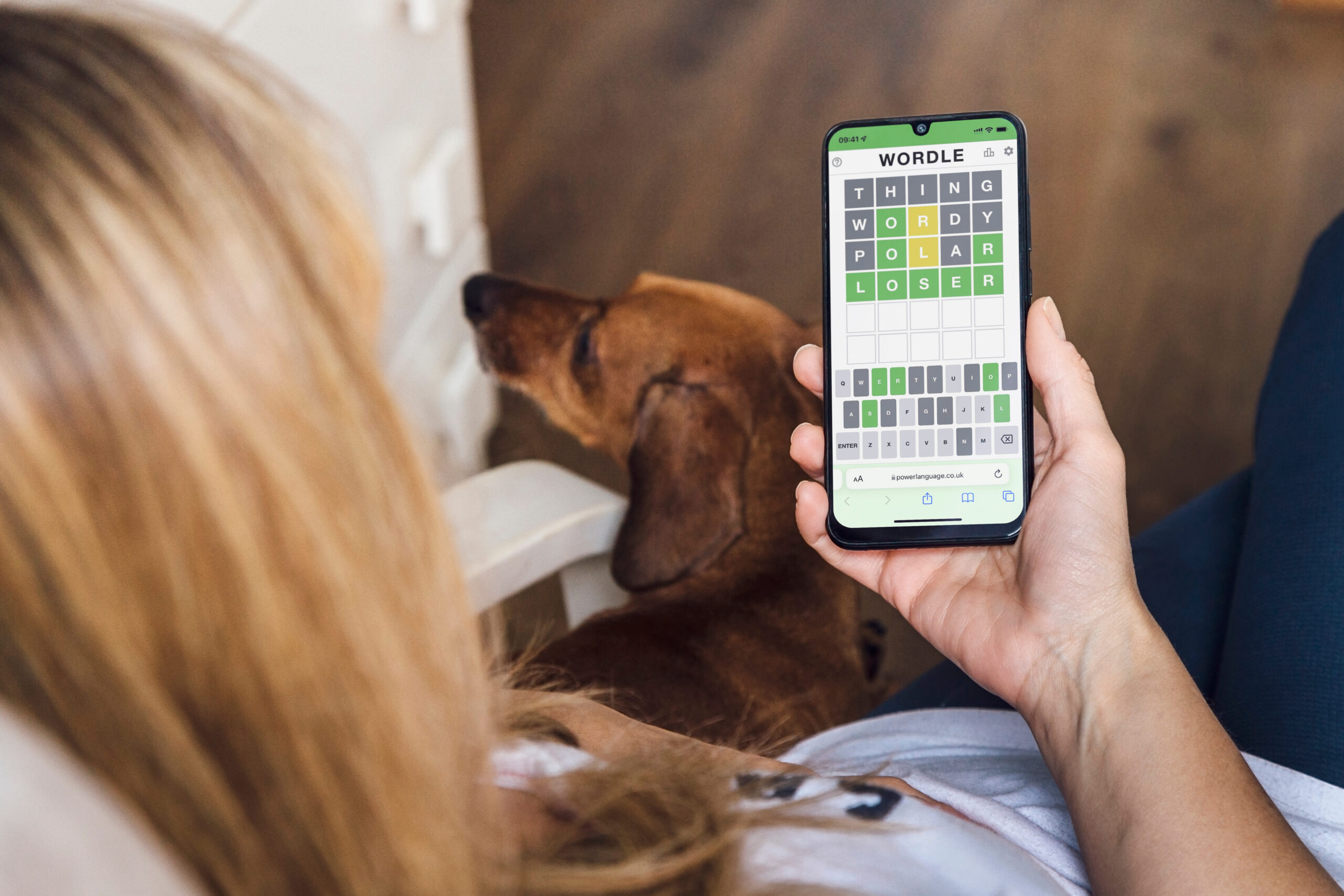 Woman comfortably at home playing Wordle on her phone. Popular word game displayed on a smartphone screen.