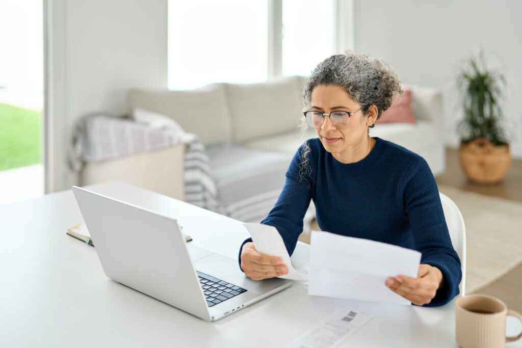 Mature lady paying bills online checking medical receipts bills using laptop.