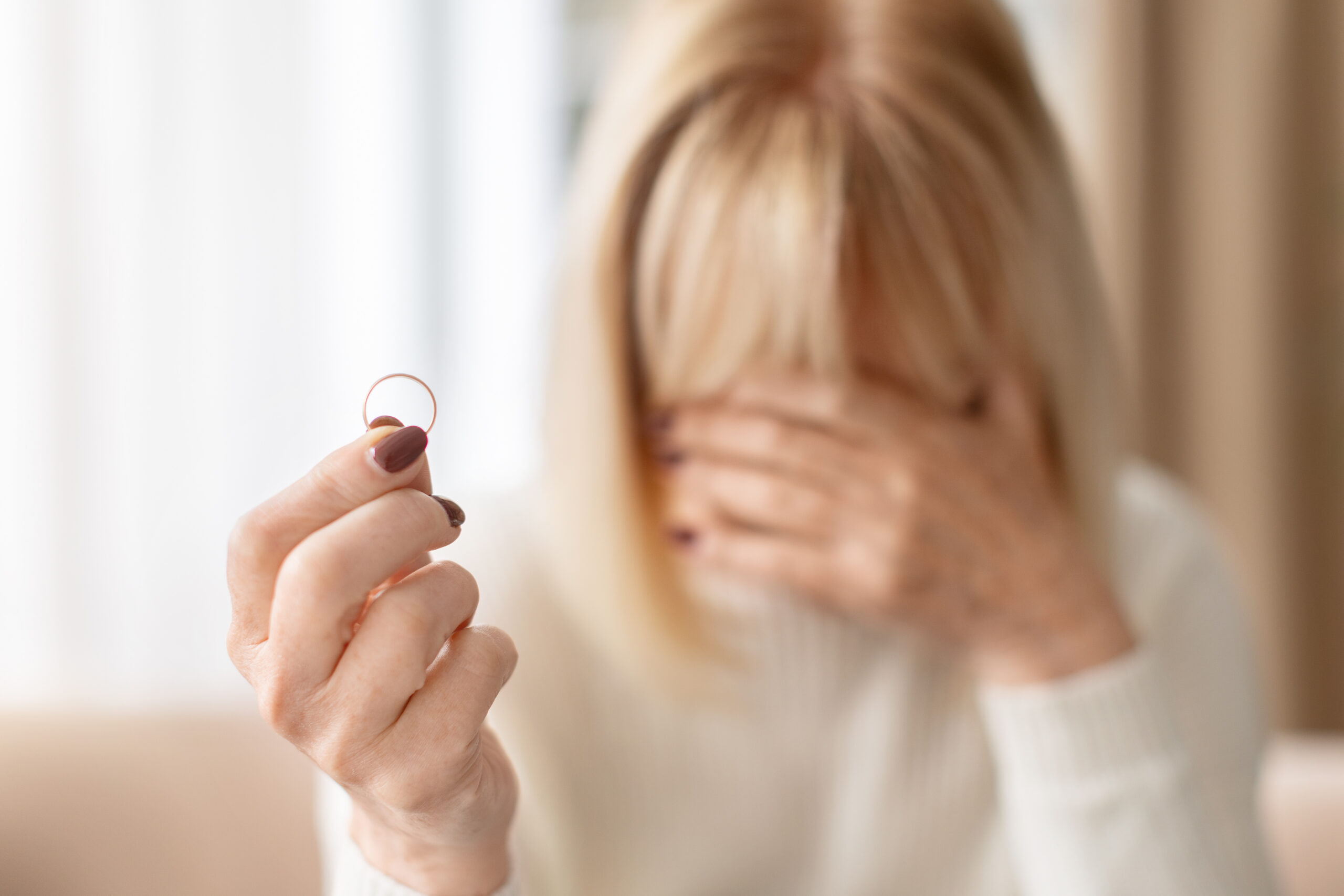 Sad senior woman holding wedding ring and covering face with hand