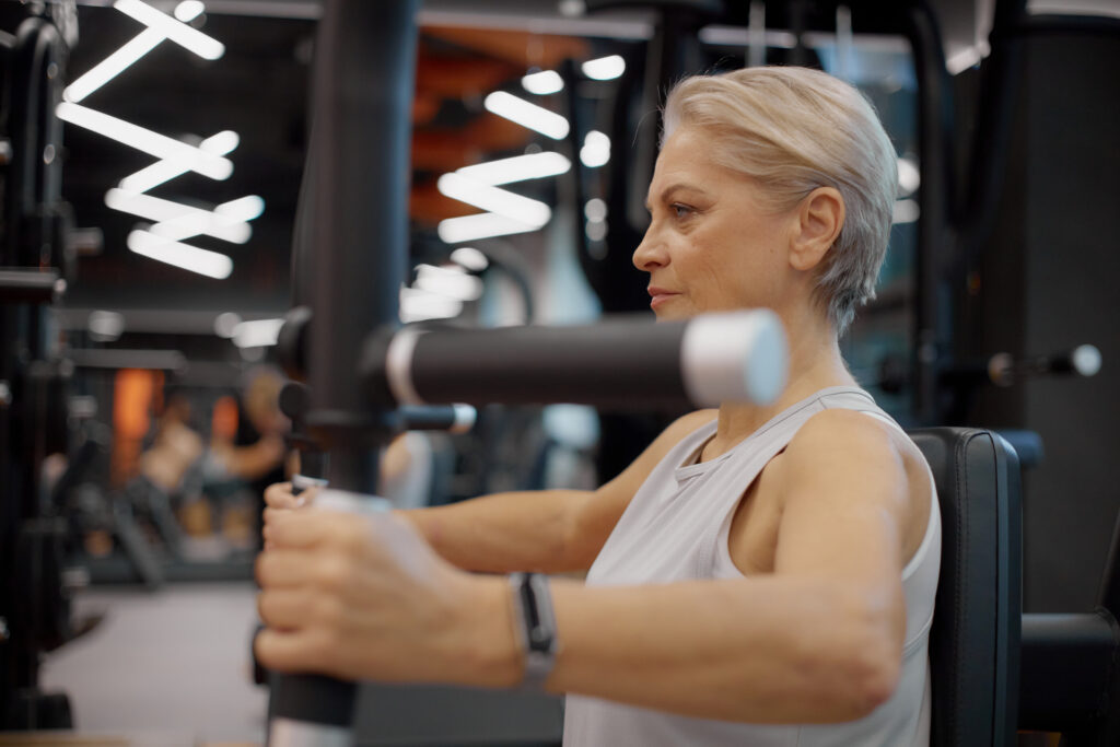 Senior Caucasian Woman Exercising on Gym Machine during Strength Training