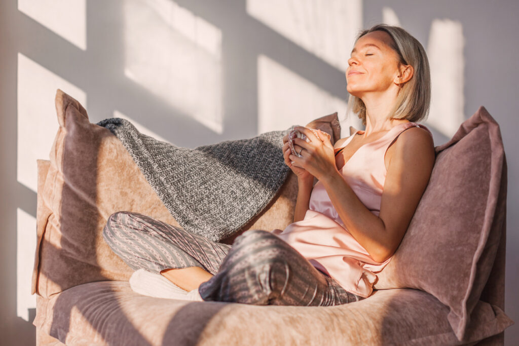 Adult midlife woman sitting on the sofa at home and having a cup of coffee, relaxation concept