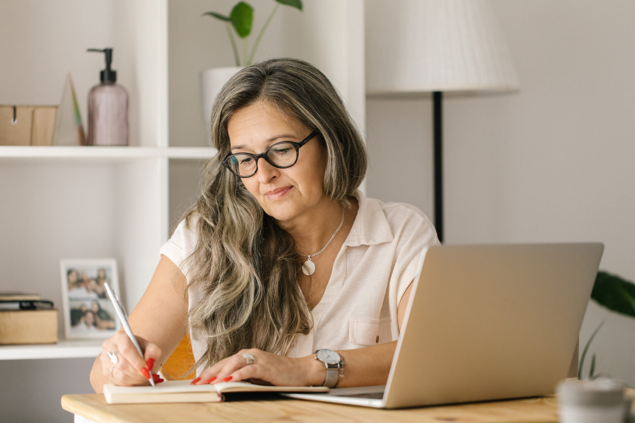 Mature woman writing down in notebook with pen at home